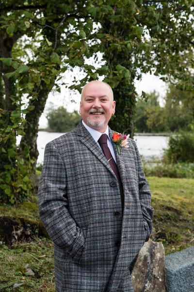 Groom stands and poses for camera in garden forest setting