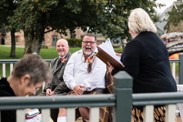 Grooms laugh during wedding ceremony with officiant