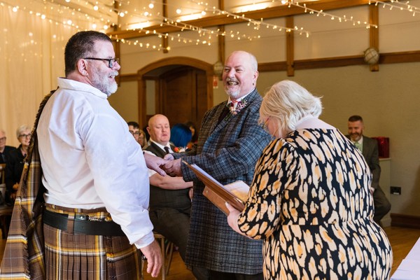 Grooms at alter with officiant in front of audience members laughing