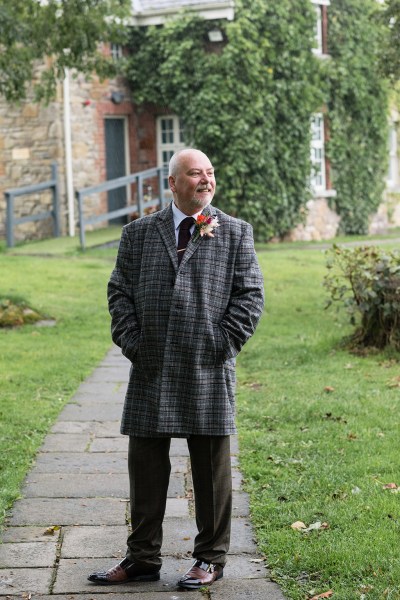 Groom stands on pathway near grass exterior shot