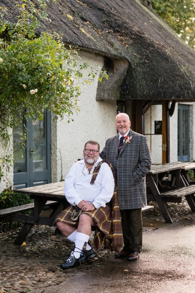 Grooms sit at picnic table bench outside of wedding venue