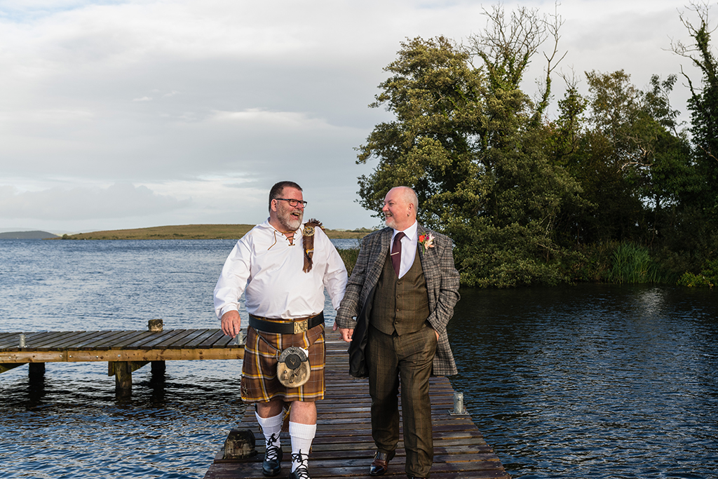 Grooms walk on boardwalk above lake setting trees in background