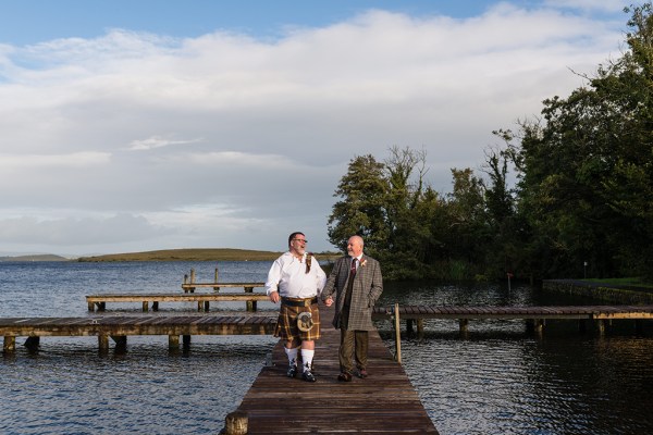 Grooms walk on boardwalk above lake setting trees in background