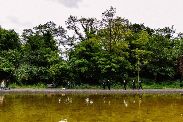 Groomsmen walking along lake in garden