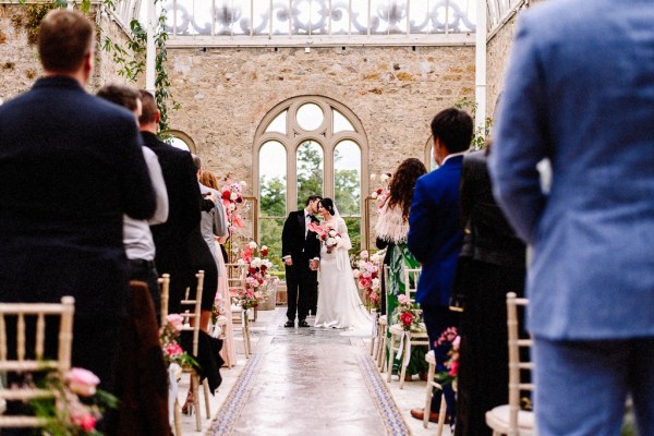 Bride and groom walk out of ceremony smiling kissing kiss