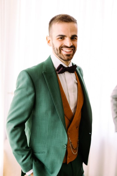 Groom in green and orange waistcoat getting ready smiles