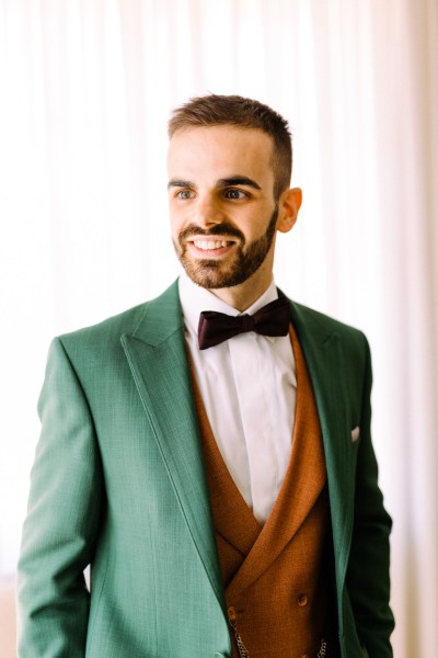 Groom in green and orange waistcoat getting ready smiles