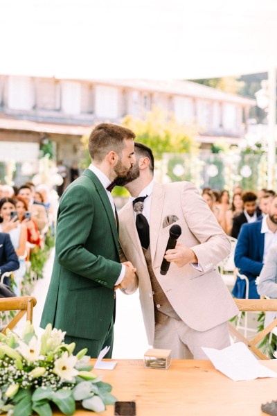 Groom holds microphone and kisses groom on cheek