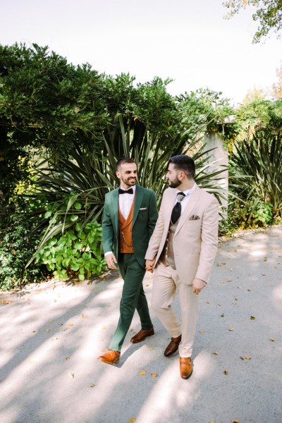 Grooms walk hand in hand outside in garden area