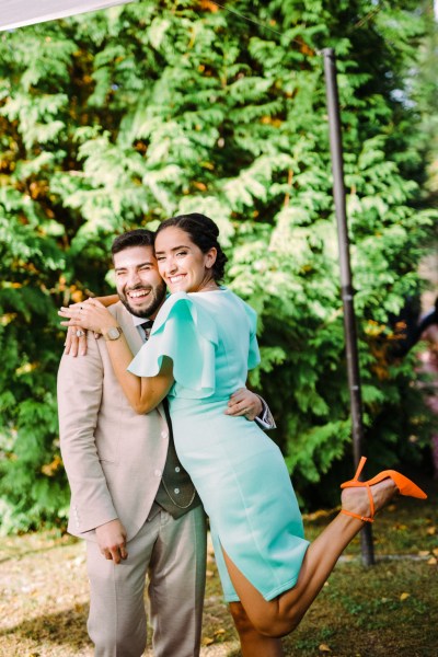 Woman in blue dress and orange heels hugs the groom