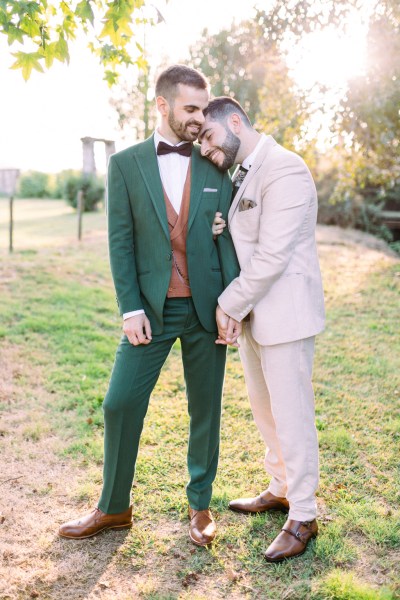 Groom leans on grooms shoulder smiles in garden park