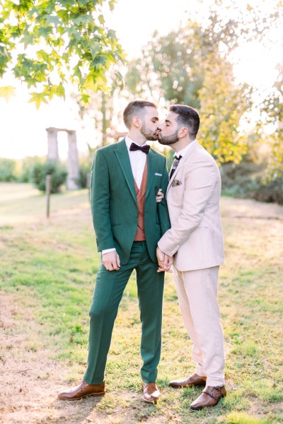 Grooms kiss in garden holding hands