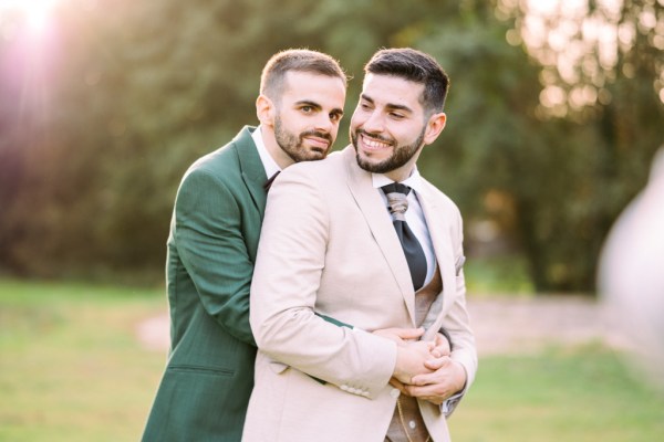 Groom hugs groom from behind in park garden