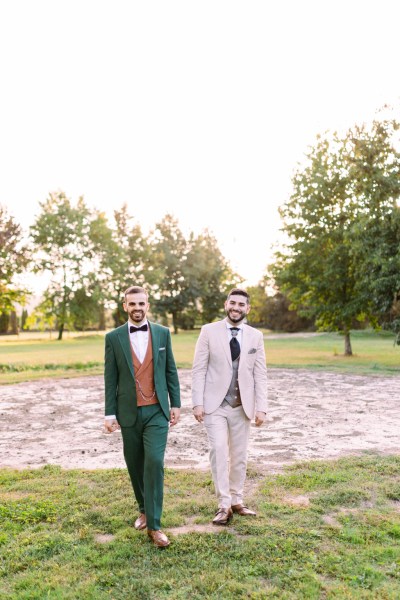 Grooms walk hand in hand in garden holding hands