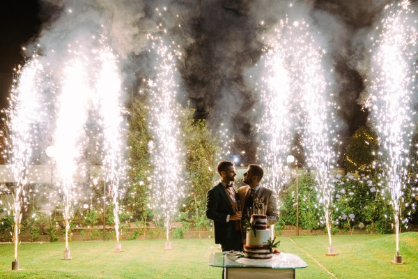 Firework display behind grooms with white cake