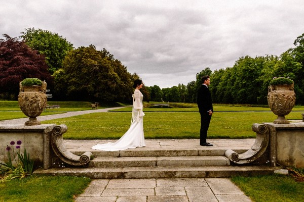 Bride approaches groom in garden grass in background