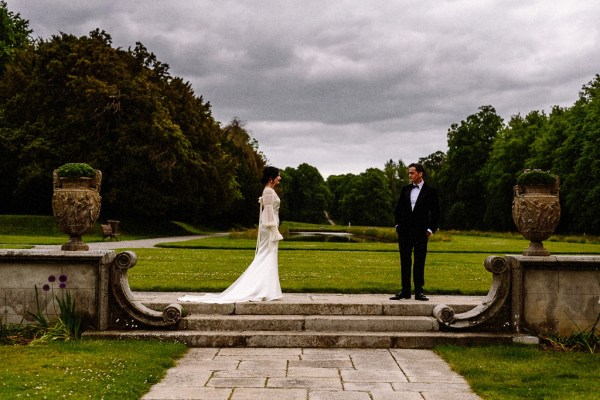 Bride approaches groom in garden grass in background