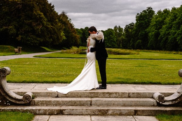 Bride approaches groom in garden grass in background they embrace on steps