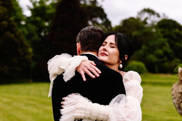 Bride approaches groom in garden grass in background they embrace on steps hug