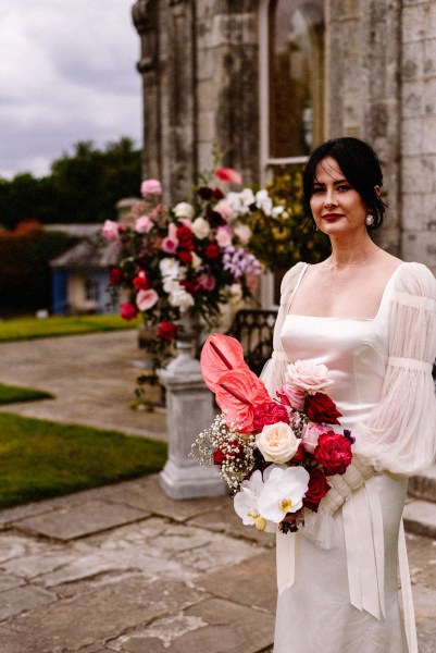 Flowers in background to bride as she holds rose bouquet