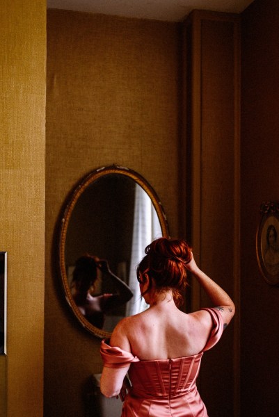 Bridesmaid looks at reflection in mirror fixing hair