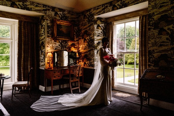 Long train detail on brides gown/dress as she looks out of mirror holding bouquet