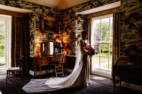 Long train detail on brides gown/dress as she looks out of mirror holding bouquet