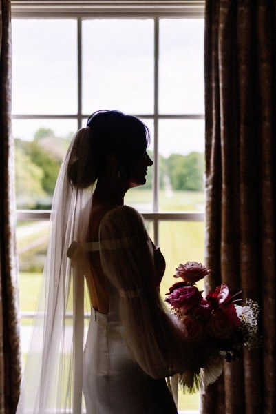 Long train detail on brides gown/dress as she looks out of mirror holding bouquet