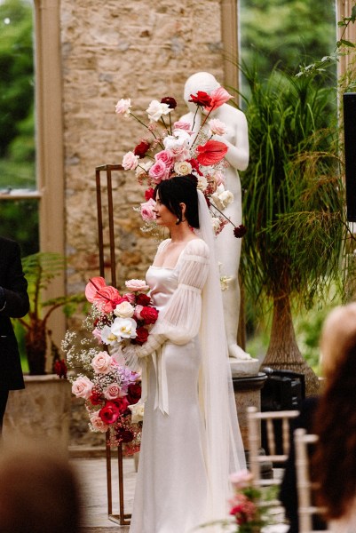 Bride at alter holding red pink roses flowers and statue