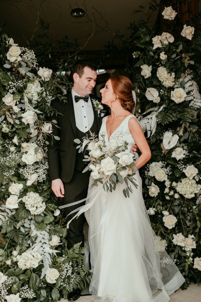 Bride and groom kissing surrounded by bed of flowers roses white bouquet looking at each other