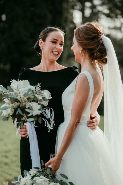 Bridesmaid sister in black and bride hugging outside garden shot