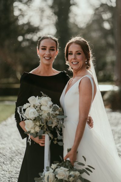 Bridesmaid sister in black and bride hugging outside garden shot