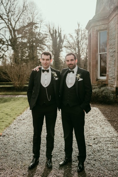 Groom and groomsman hug outside on pathway to wedding venue