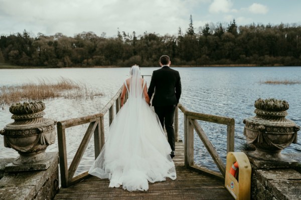 Bride and groom walk on the boardwalk towards lake