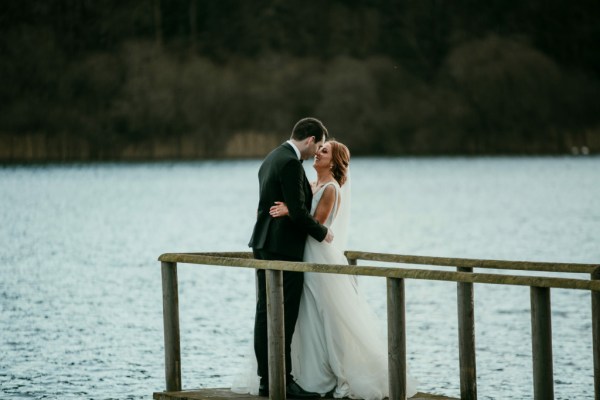 Bride and groom walk on the boardwalk towards lake kissing kiss