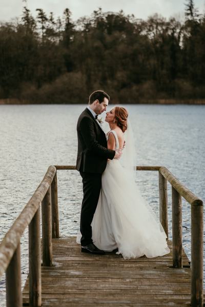 Bride and groom walk on the boardwalk towards lake hugging hug