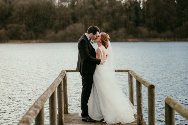 Bride and groom walk on the boardwalk towards lake kissing kiss