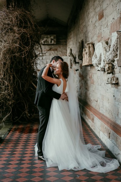 Bride on groom stand on checkered floor old rustic vibe embracing