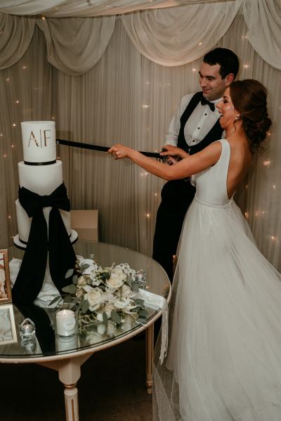 Bride and groom cut the cake with sword AF initials white