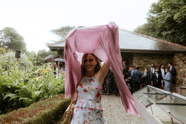 Woman holds pink scarf over head to protect from the rain