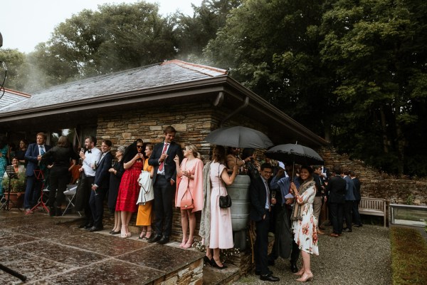 Atmosphere shot of guests under glasshouse marquee sheltering under the rain