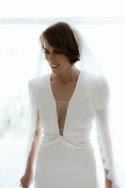 Bride stands at the window wearing veil ready for wedding