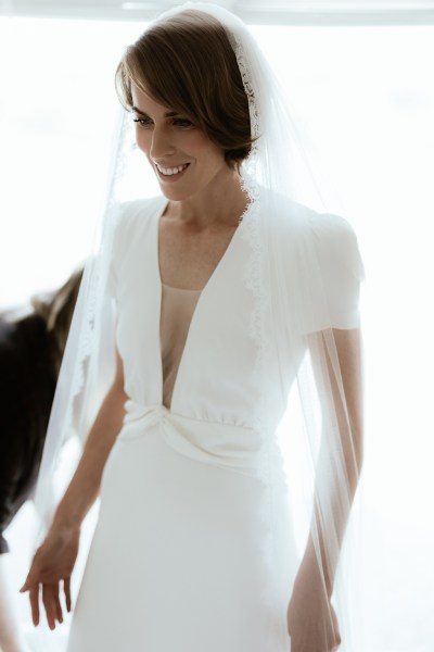 Bride stands at the window wearing veil ready for wedding