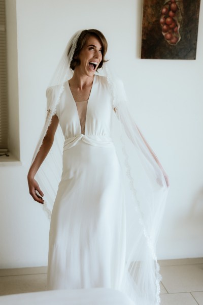 Bride stands at the window wearing veil ready for wedding