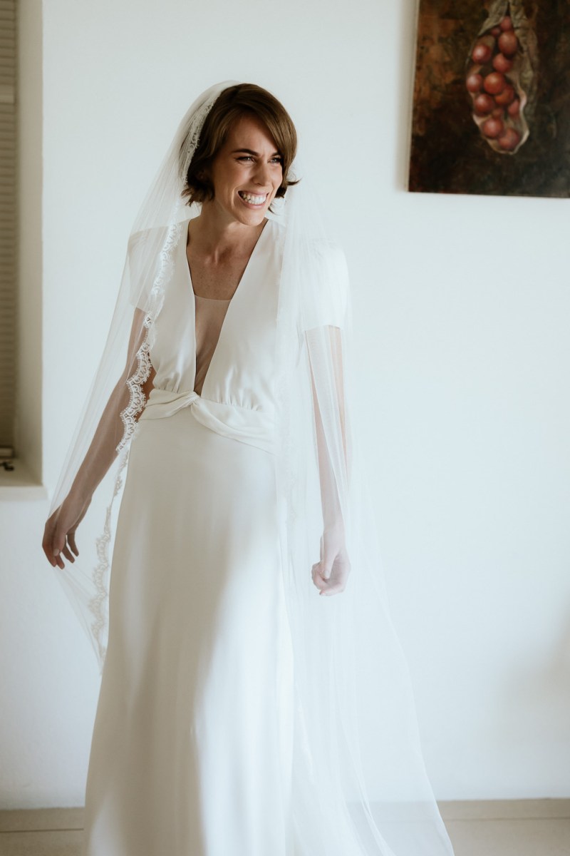 Bride stands at the window wearing veil ready for wedding smiling