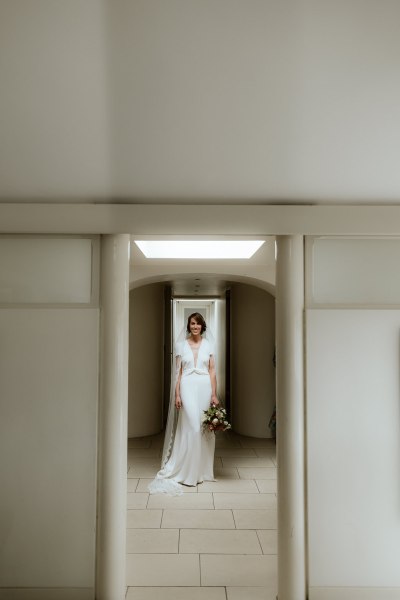 Bride stands in doorway doorframe holding bouquet