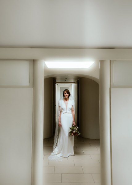 Bride stands in doorway doorframe holding bouquet