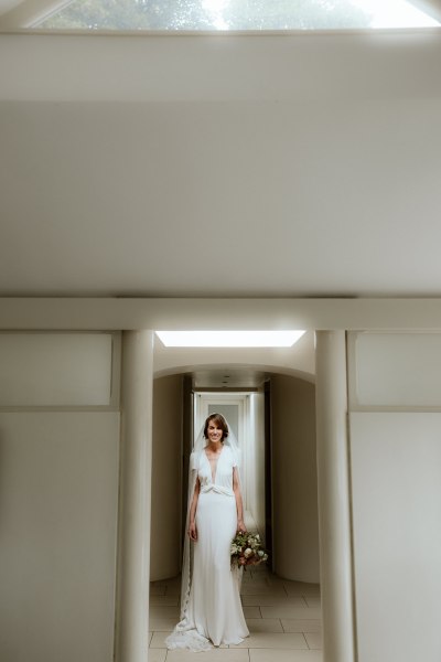 Bride stands in doorway doorframe holding bouquet