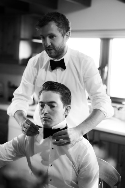 Black and white image of groom and groomsman getting ready bowtie shirts