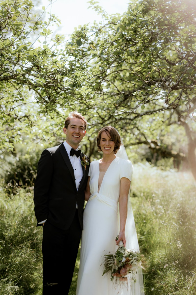 Bride and groom face the camera trees in background forest setting